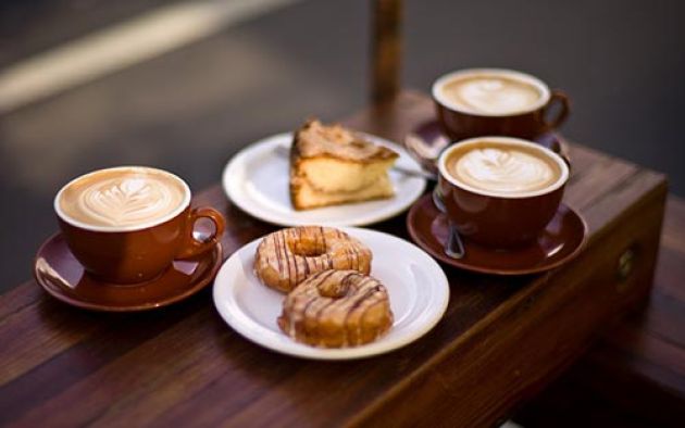 Three cups of coffee, two doughnuts and a slice of pie sitting on a wooden bench