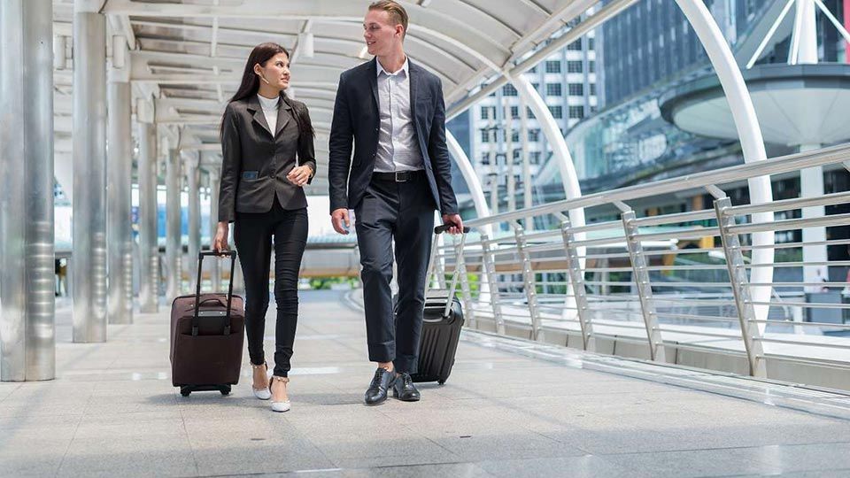 A man and a woman walking through an airport pulling a suitcase each