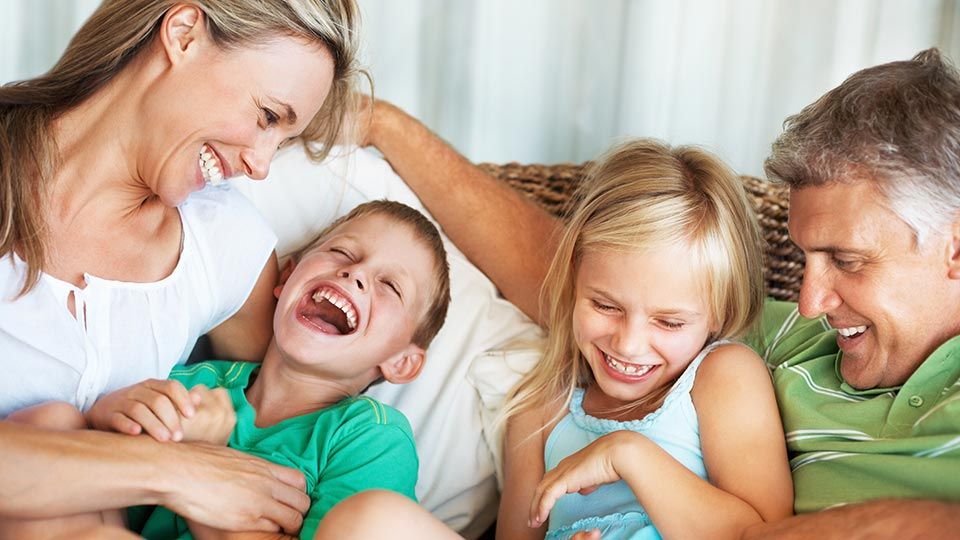 A mother & father laughing and playing with a young boy and girl on a couch