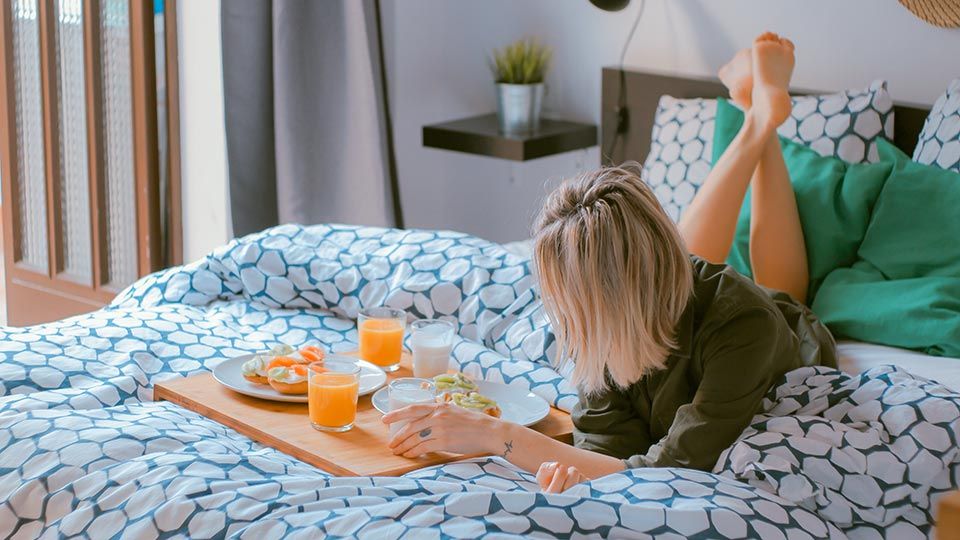 Young woman lying casually on a bed eating food from a tray