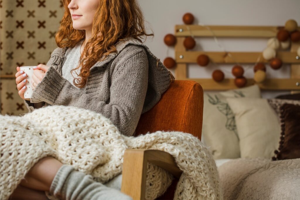 Woman with blanket sitting in chair with coffee. Affordable accommodation near Melbourne Airport without compromising comfort. Melbourne Airport accommodation, cheap and affordable